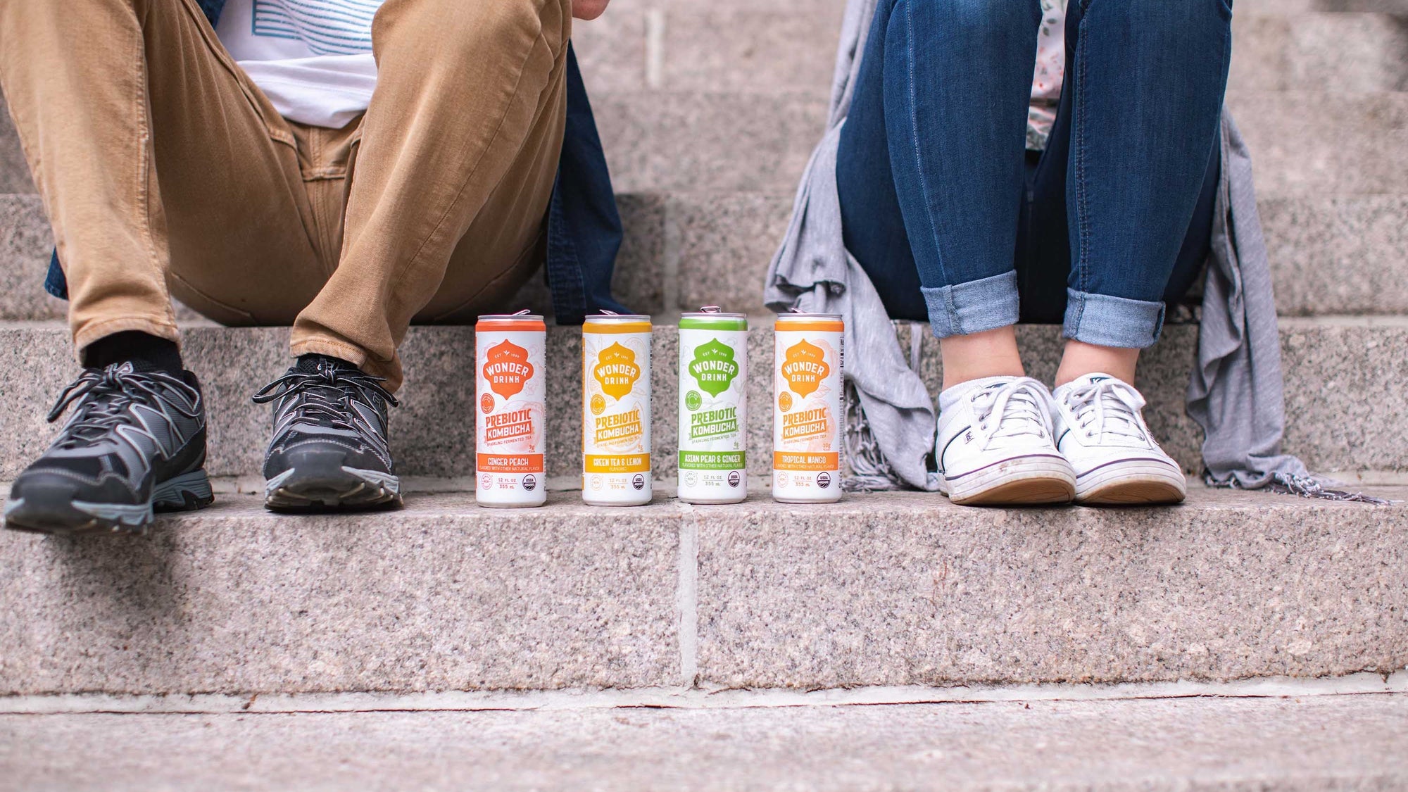 Two people sitting on public steps with cans of wonder drink between them