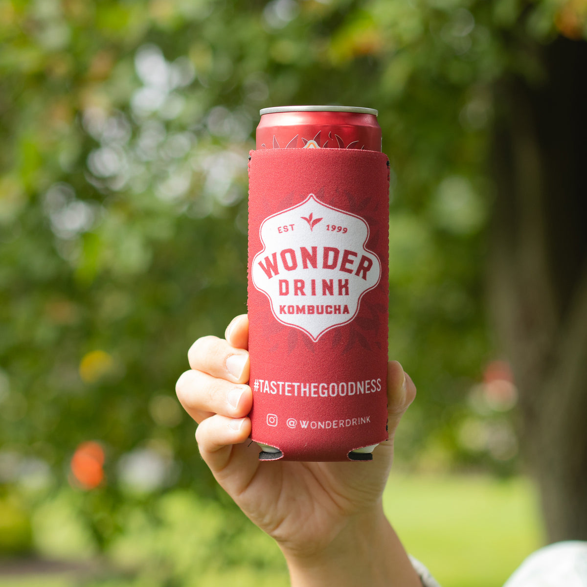 a hand holding a wonder drink kombucha in a koozie