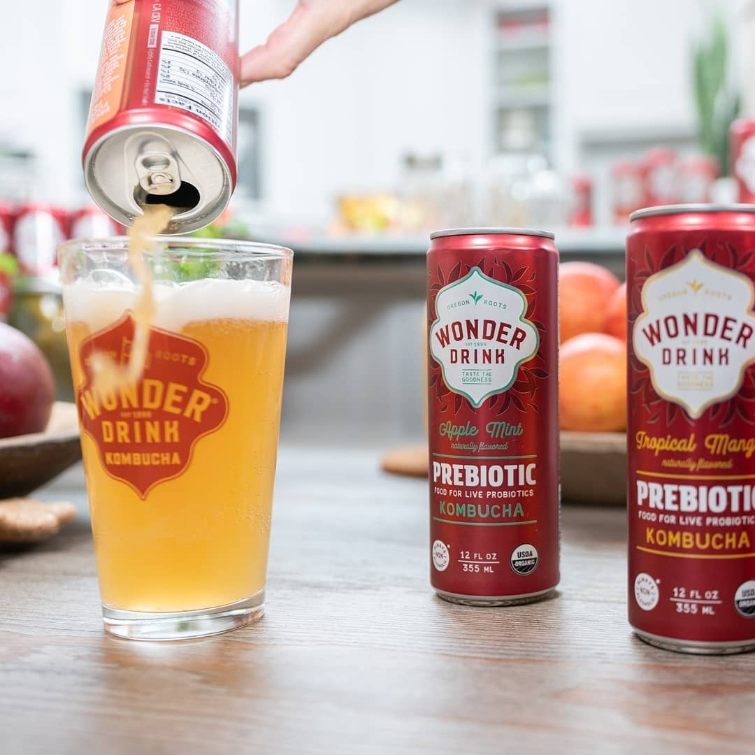 a hand pouring a wonder drink kombucha in a pint glass